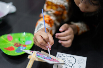 A close-up of a child’s hand painting colorful artwork with a small brush on a canvas. The scene shows bright colors and focused artistic activity.