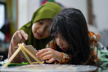 Two young girls painting together on a small easel while lying on the floor at home. They look focused and happy as they share a creative activity using brushes and bright colors.