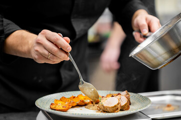 Chef plating sliced pork tenderloin with sauce and roasted potatoes in a professional restaurant kitchen, close-up