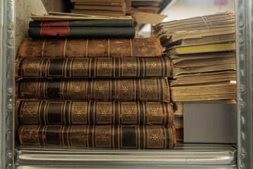 A shelf filled with antique leather-bound books and old paper documents, showing vintage spines and...