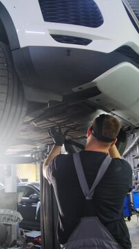 Man observes bottom of automobile to check for possible damage. Repairman looks attentively at underside of car to detect oil leaks. Vertical shot
