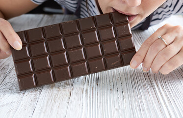 A girl eats a chocolate bar on a white wooden table. Close-up.