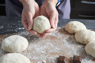 A close-up of a woman's hands kneading dough on a kitchen counter. Making vanilla buns.