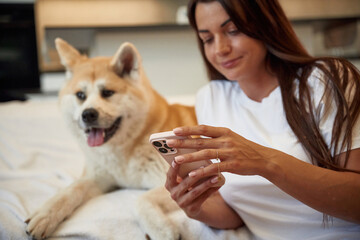 Social media conception, holding smartphone. Woman is with her Shibu Inu dog at home