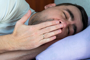 Young man sighs and covers his mouth with his hand