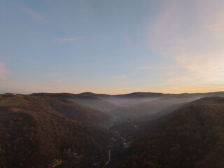 Sunrise Over Forested Hills and Winding Road in Misty Valley.