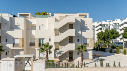 Front view of modern Mediterranean apartment building with central staircase, palm trees, and clean architectural lines © Tom