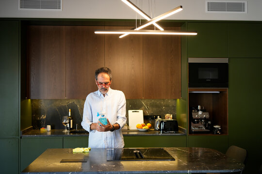 Mature man holding spray bottle cleaning modern kitchen