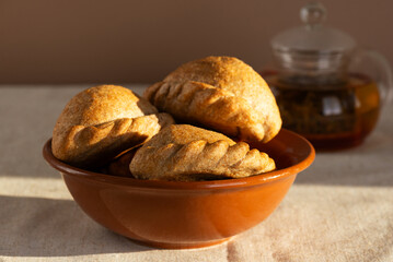Traditional homemade pies with cabbage in a clay bowl with tea on a table. Cozy food.