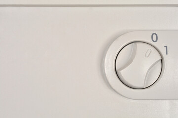 A close-up shows a gray plastic rotary switch marked '0' and '1', with the dial clearly turned to the '0' or 'Off' position on a pale appliance panel