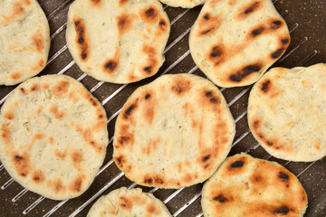 A close-up, top-down view shows several round flatbreads with golden-brown marks being cooked directly on the dark ribbed surface of a grill pan