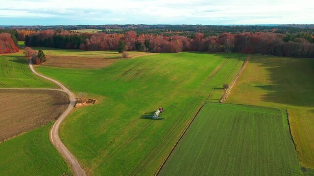 Aerial view of vibrant green farm fields contrasted by a winding dirt road and colorful autumn trees, creating a picturesque landscape, Andechs, Bayern, Germany.
