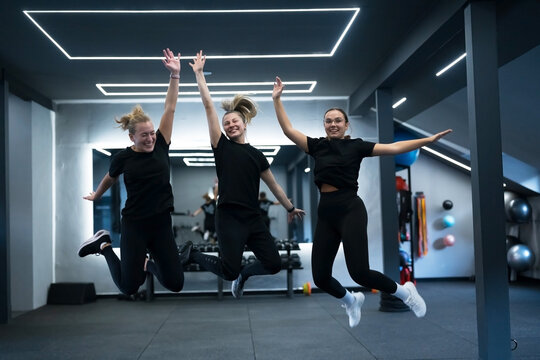 Group of women joyfully jump in a gym during a fitness class in the afternoon - Powered by Adobe
