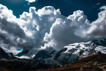 Dramatic cumulonimbus clouds hovering over snow capped mountain peaks under a deep blue sky with sunlight breaking through