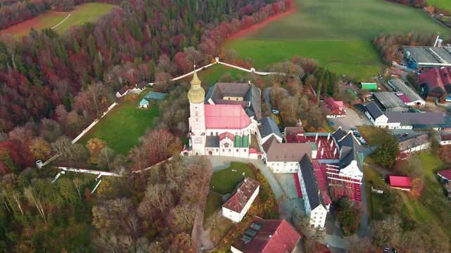 Aerial view of Andechs Abbey, a symphony of red roofs and golden spires, nestled amidst the autumn colors of the surrounding trees, Andechs, Bayern, Germany.