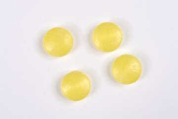 Four round, translucent yellow hard candies with visible surface lines are scattered in a small group on a plain white background