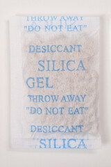 A vertical close-up of a white desiccant silica gel packet featuring prominent blue 