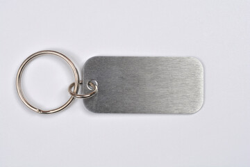 A horizontally positioned, rectangular brushed metal keychain tag with an attached silver split key ring, showing its textured surface, isolated on a white background