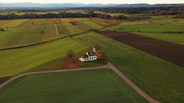 Aerial view of a white church with an orange roof surrounded by green and brown fields under a blue sky, Raisting, Bayern, Germany.