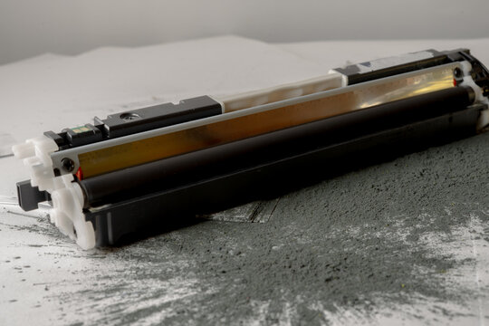 Printer toner cartridge placed on sheets of white paper and scattered with toner powder