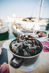 Fresh mussels served in a pot at a marina restaurant, capturing the vibrant atmosphere of a seaside dining experience on a sunny day