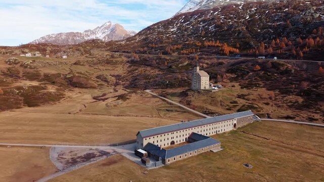Aerial view of the Simplon Hospice, a historic building amidst the brown fields, with snowy mountains as a backdrop, Simplon Hospice, Wallis, Switzerland.