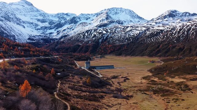 Aerial view of the Simplon Hospice nestled amidst the rugged terrain, where snow-capped mountains provide a stunning contrast to the golden hues, Simplon Hospice, Wallis, Switzerland.