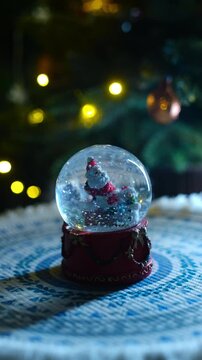 Vertical video. Hand shaking Christmas snow globe with Santa Claus and snowflakes. Christmas home decor with festive cozy atmosphere