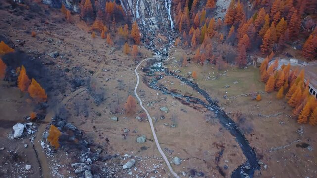 Aerial view of the Cascata del Toce, a stunning waterfall surrounded by vibrant autumn trees and a winding path, Formazza, Piedmont, Italy.