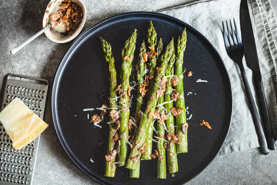 Baked asparagus with almond petals and parmesan cheese on black plate