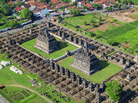 Aerial view of the ancient Plaosan Temple complex, with its weathered stone structures contrasting against vibrant green lawns, Klaten Regency, Jawa Tengah, Indonesia.