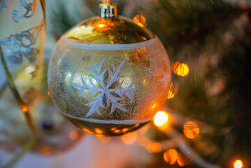A beautiful golden Christmas ball with a painted snowflake on a Christmas tree. Shot close-up, against a bokeh of yellow lights.
