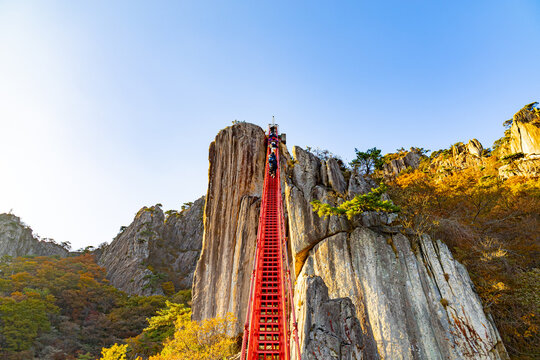 Hikers ascending a steep red stairway attached to massive rock cliffs at Daedunsan in South Korea