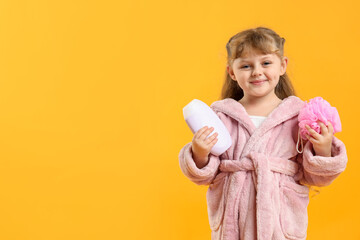 Happy girl in bathrobe with loofah and cosmetic product on yellow background. Space for text