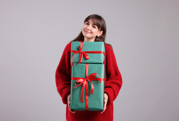 Fototapeta premium Beautiful woman in red sweater with gift boxes on grey background. Christmas and New Year celebration
