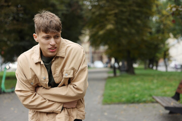Young man suffering from stomachache and nausea outdoors. Space for text