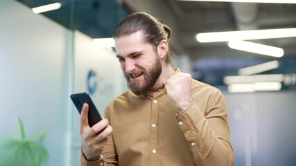 Happy excited businessman received great news on mobile phone standing in modern business office. Smiling shocked surprised entrepreneur reads a positive good message, celebrates success. Close up - Powered by Adobe