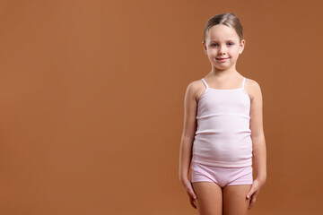 Little girl in underwear on brown background. Space for text