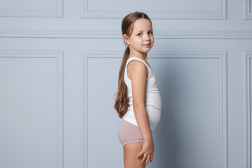Little girl in underwear near light wall. Space for text