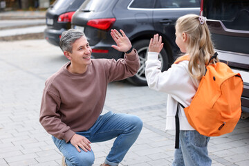 Father taking his daughter to school and giving high five near car outdoors