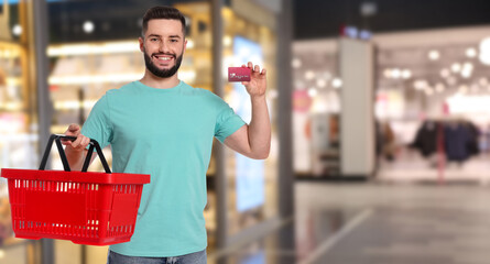 Happy man with credit card holding empty shopping basket at supermarket. Banner design