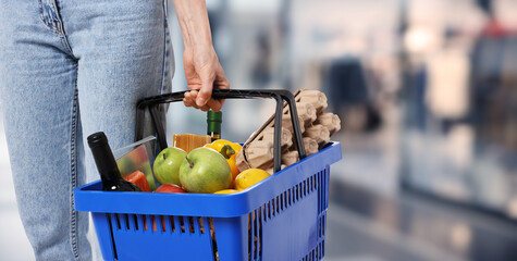 Customer holding shopping basket with different food products at supermarket, closeup. Banner design