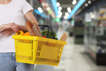 Customer holding shopping basket with different food products at supermarket, closeup