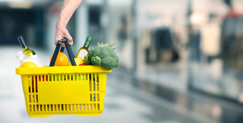 Customer holding shopping basket with different food products at supermarket, closeup. Banner design
