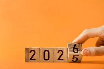 New Year. Man flipping cube with numbers 5 and 6 to make 2026 on orange background, closeup