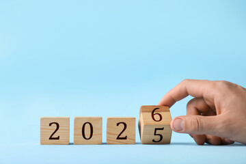 New Year. Man flipping cube with numbers 5 and 6 to make 2026 on light blue background, closeup