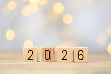 New 2026 year. Cubes with numbers on wooden table against blurred festive lights