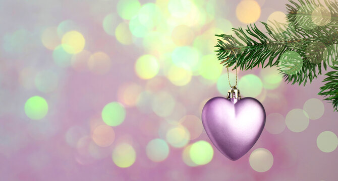 Christmas ornament in shape of heart hanging from fir tree branch against blurred lights on pink background, bokeh effect. Banner design