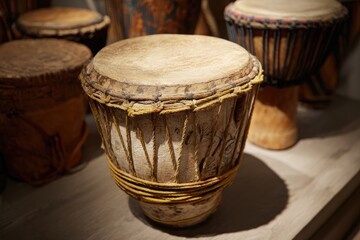 Several handmade, wooden percussion instruments with taut skins rest on a light wooden surface