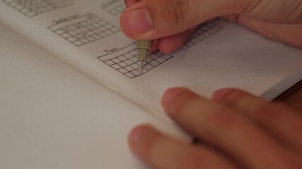 Close-up static shot of a hand and pen filling out habit tracker grid inside journal spreadsheet.